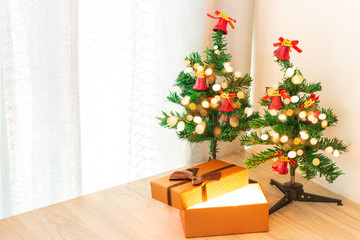 Two small Christmas trees And the gift box that was opened There is light coming from inside the box. On a wooden table that is placed in the corner of the room.