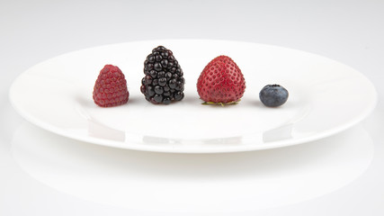 Blackberries, raspberries, blueberries and strawberries on a white plate.  Healthy and vitamin food.