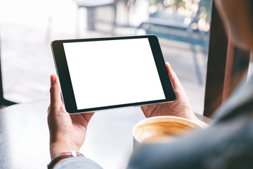 Mockup image of a woman holding black tablet with white blank screen and coffee cup on the table