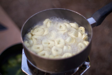 Using a canned propane travel stove to cook tortellini pasta in a pot of boiling water while camping