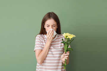 Young woman suffering from allergy to flowers on color background