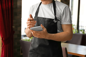 Young male waiter with notebook in restaurant, closeup