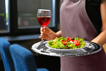 Waitress with glass of wine and dish in restaurant, closeup