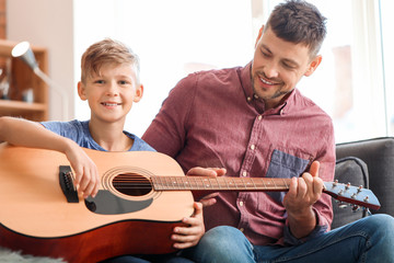 Father teaching his little son to play guitar at home