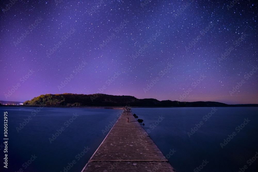 Poster beautiful shot of a long wooden pier in the center if a lake under the sky full of stars