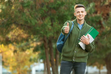 Fototapeta premium Portrait of teenage male student showing thumb-up outdoors