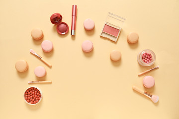 Tasty macarons with makeup cosmetics on color background