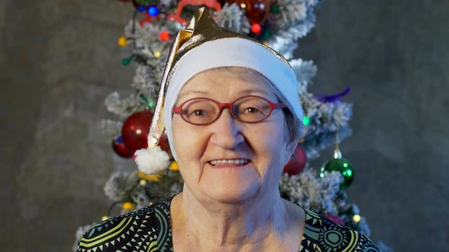Extravagant old woman with gray hair and wrinkles in glasses. Senior citizen in santa claus hat. Concept of domineering and funny elderly mother in law. Christmas Eve