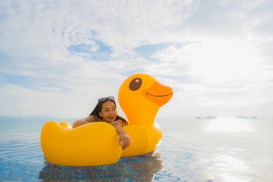 Portrait young asian woman on inflatable float yellow duck around outdoor swimming pool in hotel and resort