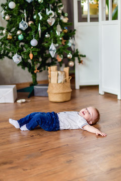 Christmas and new year. A little boy in blue jeans and a shirt lying on the floor against the Christmas tree. Vertical photography