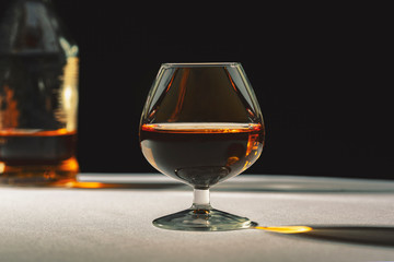 Brandy glass filled with half alcoholic drink on a black background in a beautiful light.
