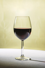 Glass goblet with red wine on a white tablecloth and on a beige background.