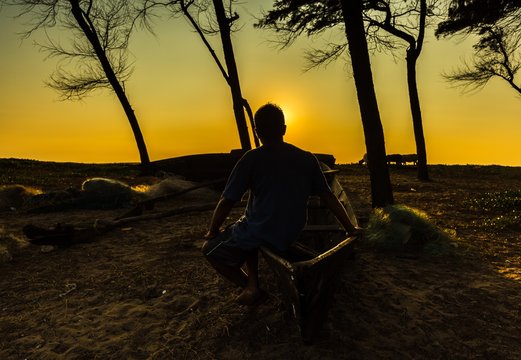 silhouette of a man sitting on a boat looking at evening sun, Pollem, Goa, India