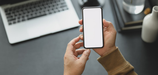Cropped shot of man holding blank screen smartphone while working on his project