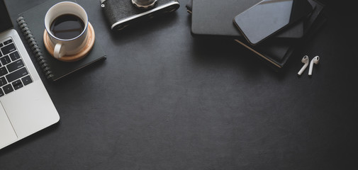 Top view of dark trendy workspace with laptop computer, coffee cup and office supplies