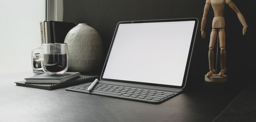 Cropped shot of modern workplace with blank screen tablet with office supplies with black wall