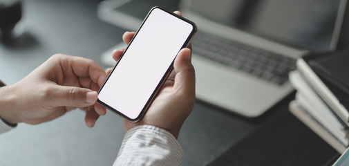 Cropped shot of professional businessman holding blank screen smartphone in dark modern office
