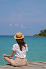 Young woman in a hat sits on a pier near the clear turquoise sea