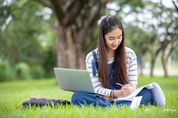 beautiful Asian girl student holding books and smiling at camera and learning and education concept  on park in summer for relax time