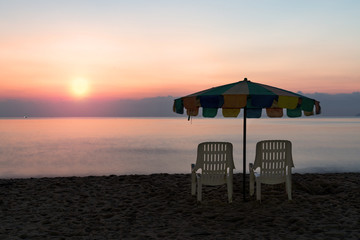 White beach chair and umbrella on tropical beach with orange sky