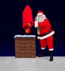 Santa Claus standing at a snowy roof and throw gifts from bag into the chimney, background of dark blue with stars. Santa upturn sack with christmas boxes to chimney.