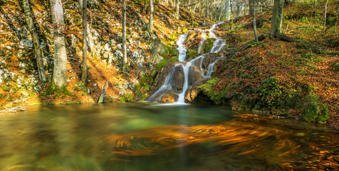 Brigth and warm colors and a beautiful stream and waterfalls in a wild mountain location in autumn