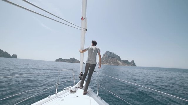 Beautiful white yacht breaks the waves. Man stands on the bow of the yacht. Clear blue water. Splashes from waves explode in different directions