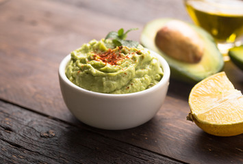 Bowl of green hummus, delicious cream of chickpeas and avocado on a wood background.