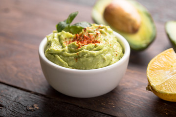 Bowl of green hummus, delicious cream of chickpeas and avocado on a wood background.