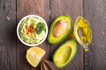 Bowl of green hummus, delicious cream of chickpeas and avocado on a wood background.