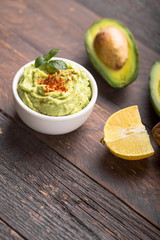 Bowl of green hummus, delicious cream of chickpeas and avocado on a wood background.