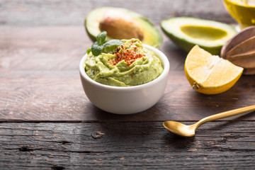 Bowl of green hummus, delicious cream of chickpeas and avocado on a wood background.