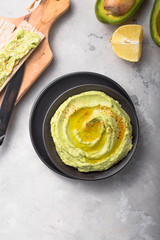 Bowl of green hummus, delicious cream of chickpeas and avocado on a stone  background.