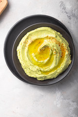 Bowl of green hummus, delicious cream of chickpeas and avocado on a stone  background.