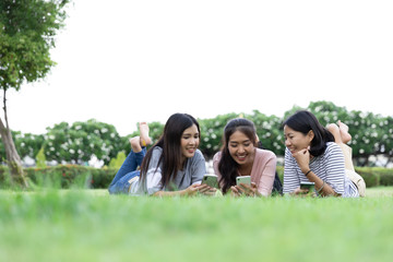 Happy young Asian woman three people using phone surf internet while laying down on grass together. lifestyle, Communication and technology concept. with Copy space
