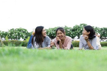 Group Cheerful young Asian woman in casual clothes three people laying down on grass laughing and talk together in the park. Happy vacations. with Copy space