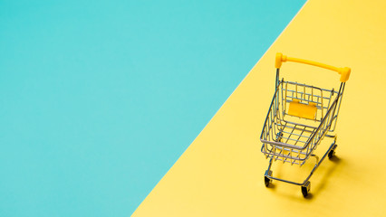 Empty miniature shopping cart on blue and yellow background. Toy trolley on bright colorful background, copy space for text or design. - Powered by Adobe