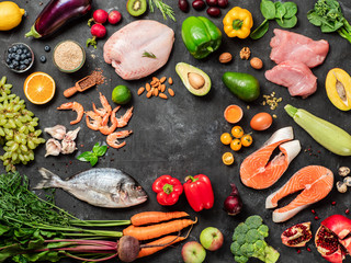 Pegan diet conept with copy space in center. Vegan plus paleo diet food ingredients - vegetables, fruits, raw meat and fish on dark background. Top view or flat lay
