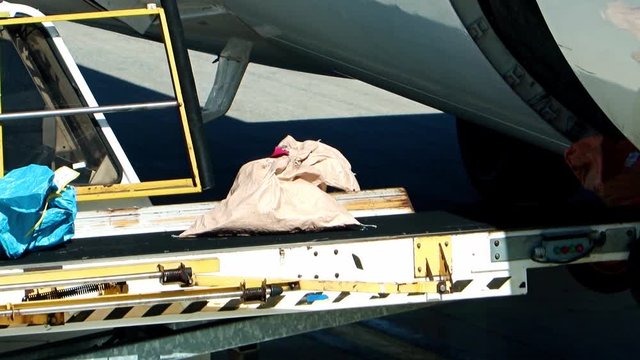 Unloading the saks from the fuselage of aircraft. The bags ride on the conveyor when unloading the air plane on the airport.