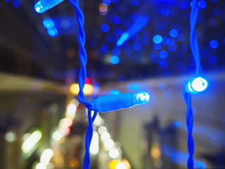 Blurred image of café window  in the dark. Christmas theme with blue garland. Bokeh of streetlights. Abstract background. Soft focus.