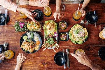 Group of people having dinner with various traditional Asian dishes and drinks, view from above