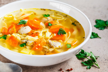 Chicken noodle soup with parsley and vegetables in a white plate.