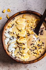 Chocolate smoothie bowl with coconut chips, banana and cocoa nibs in wooden bowl, top view. Healthy vegetarian breakfast concept.