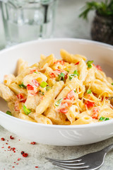 Penne pasta with chicken, pepper and green onions in creamy sauce in a white plate, gray background.