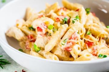 Penne pasta with chicken, pepper and green onions in creamy sauce in a white plate, gray background.