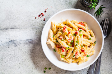 Penne pasta with chicken, pepper and green onions in creamy sauce in a white plate, gray background, top view. - Powered by Adobe