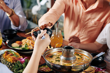 Hand of child taking delicious skewers with chopsticks when sitting at dinner table with relatives