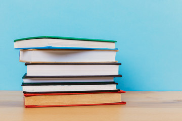 A simple composition of many hardback books, raw books on a wooden table and a bright blue background