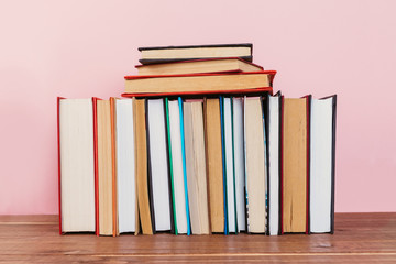 A simple composition of many hardback books, raw books on a wooden table and a pale pink background