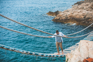 man walking by suspension bridge cross sea bay